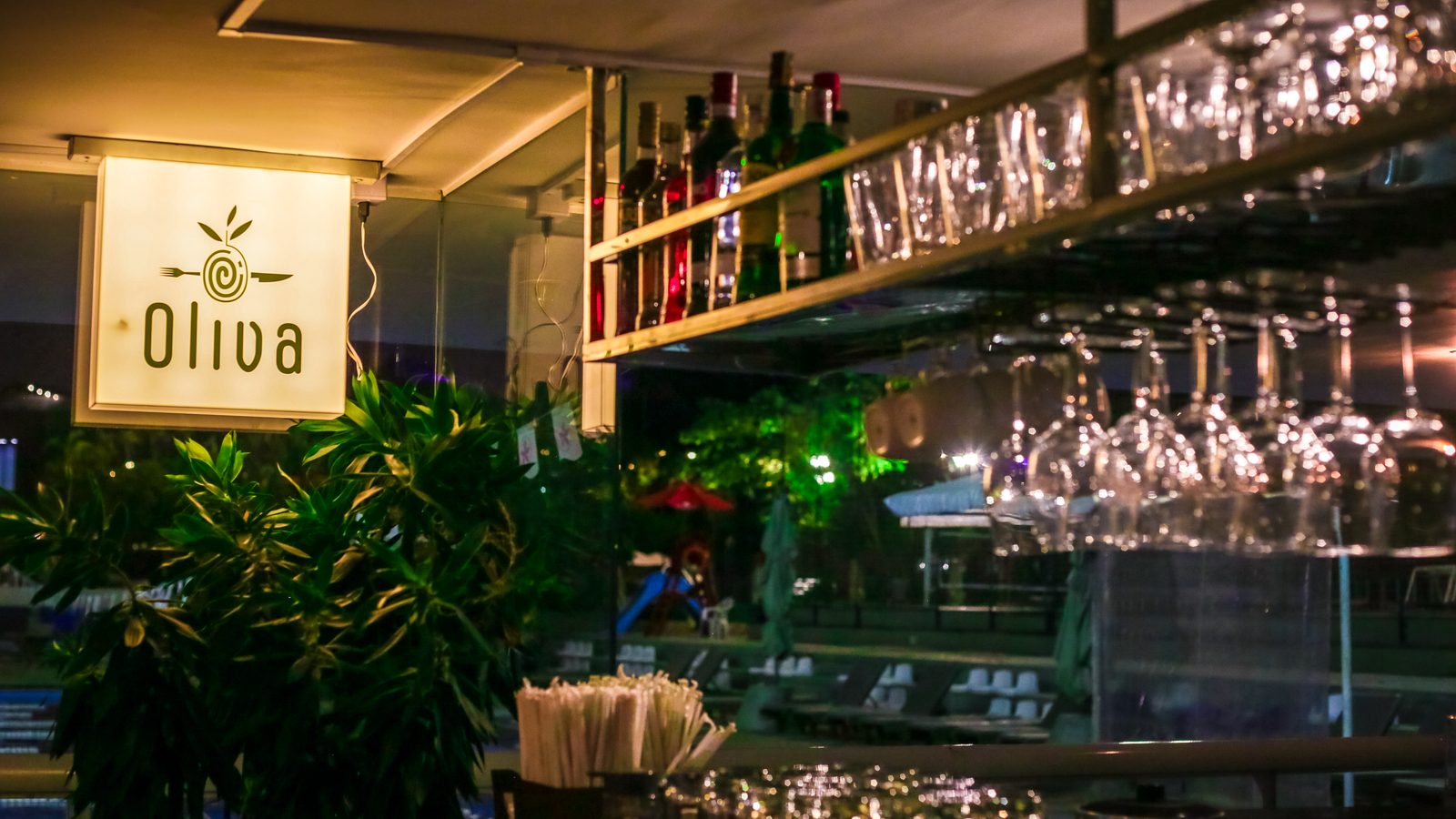 Fachada do restaurante Oliva com letreiro iluminado e plantas