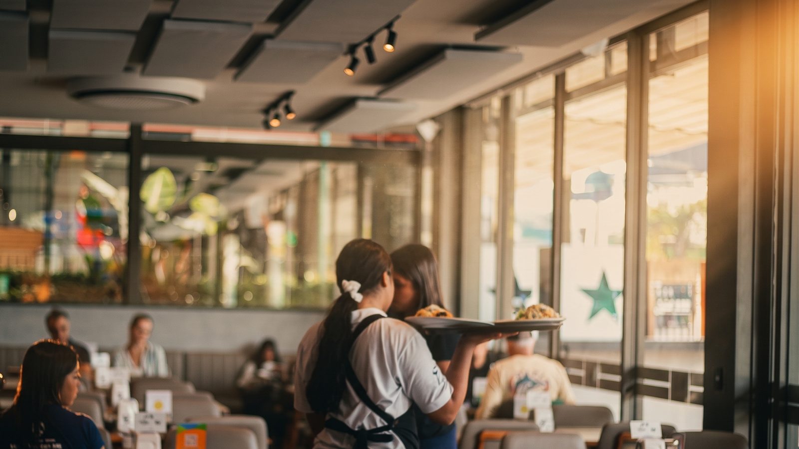 Garçonete servindo pratos em restaurante iluminado pelo sol da tarde