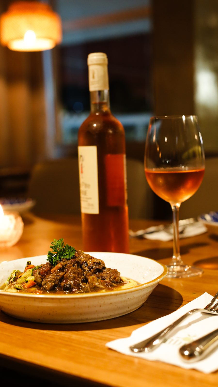 Taça de vinho rosé ao lado de prato de carne com risoto